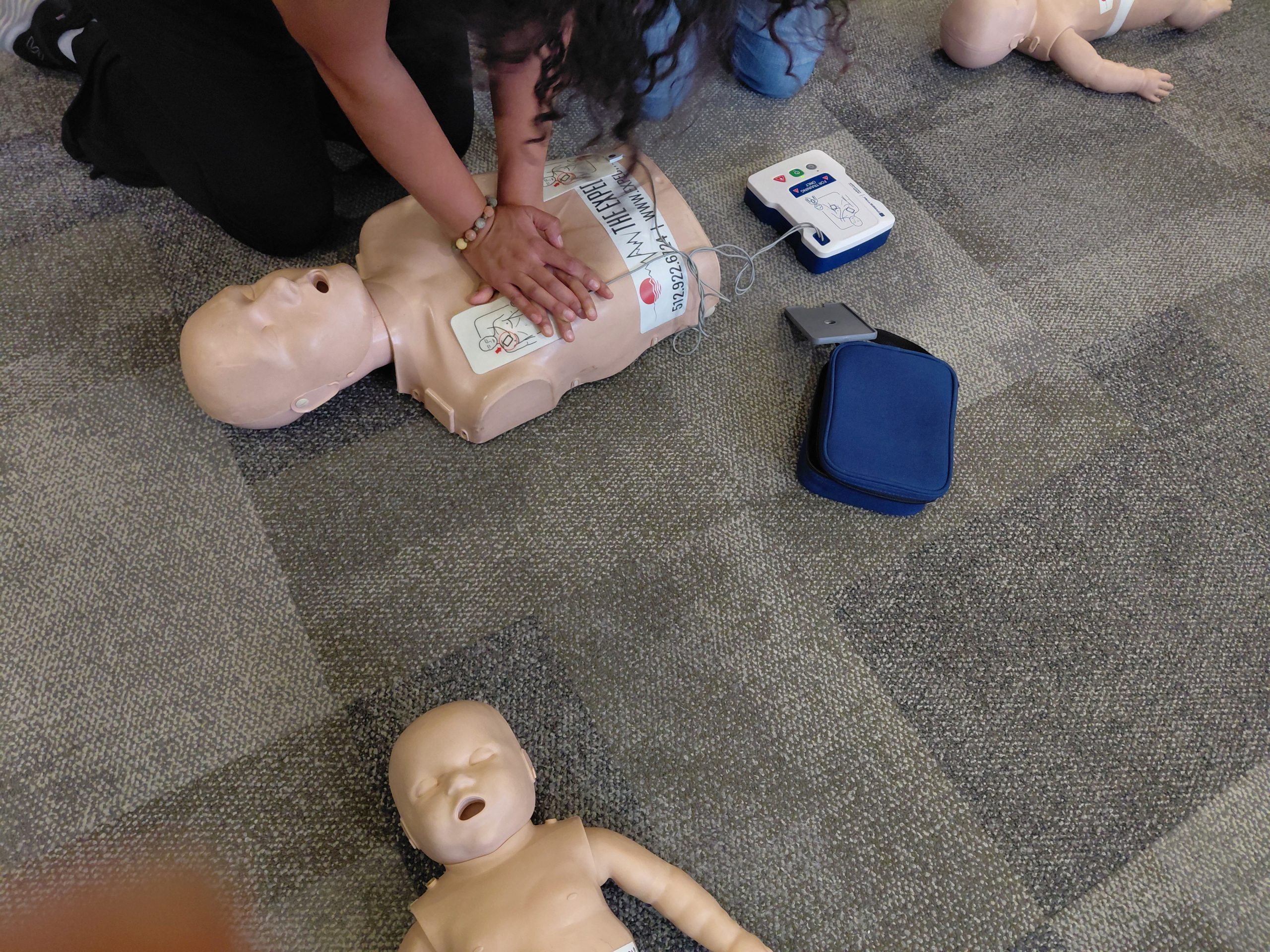 Close-up of a student practicing CPR compressions on an Expedition School<br />
branded training mannequin with an AED training device placed beside it during the<br />
Wilderness First Aid course.